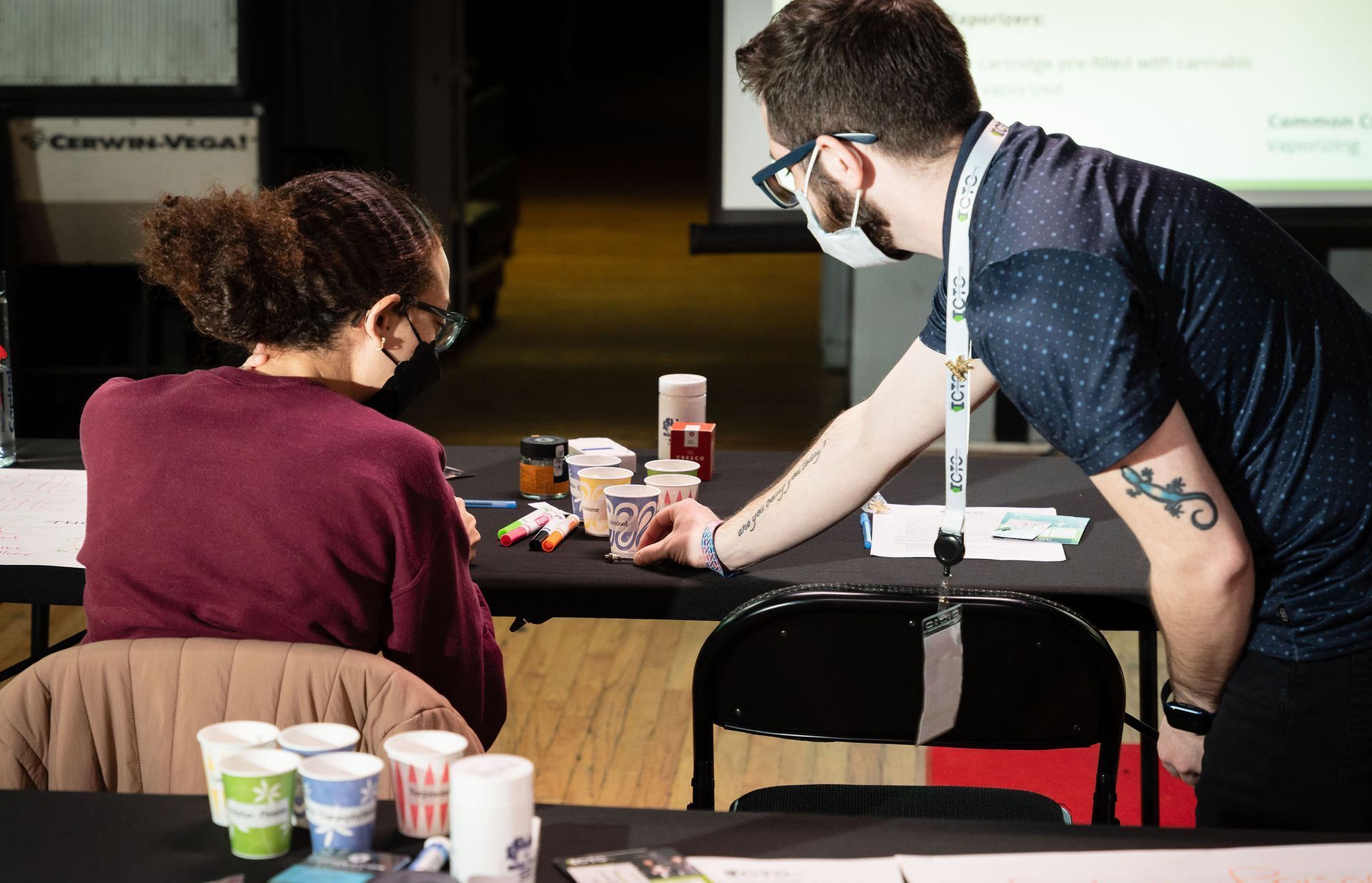 A man and a woman are sitting at a table with cups on it.