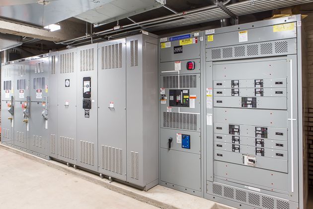 Large gray electrical switchgear cabinets in an industrial room with control panels and warning labels