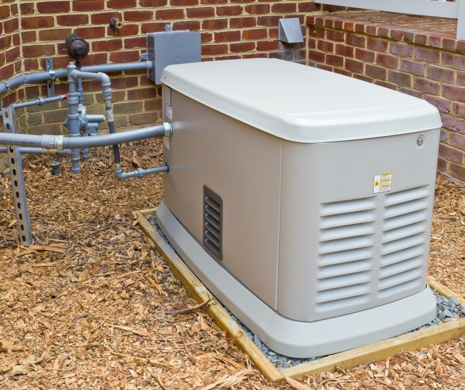 Outdoor standby generator beside a brick house, sitting on a concrete pad with wood mulch around it.