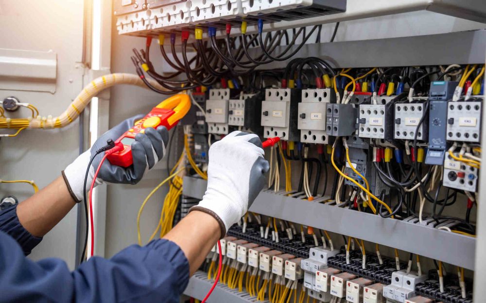 Technician testing electrical control panel with multimeter in a wiring cabinet
