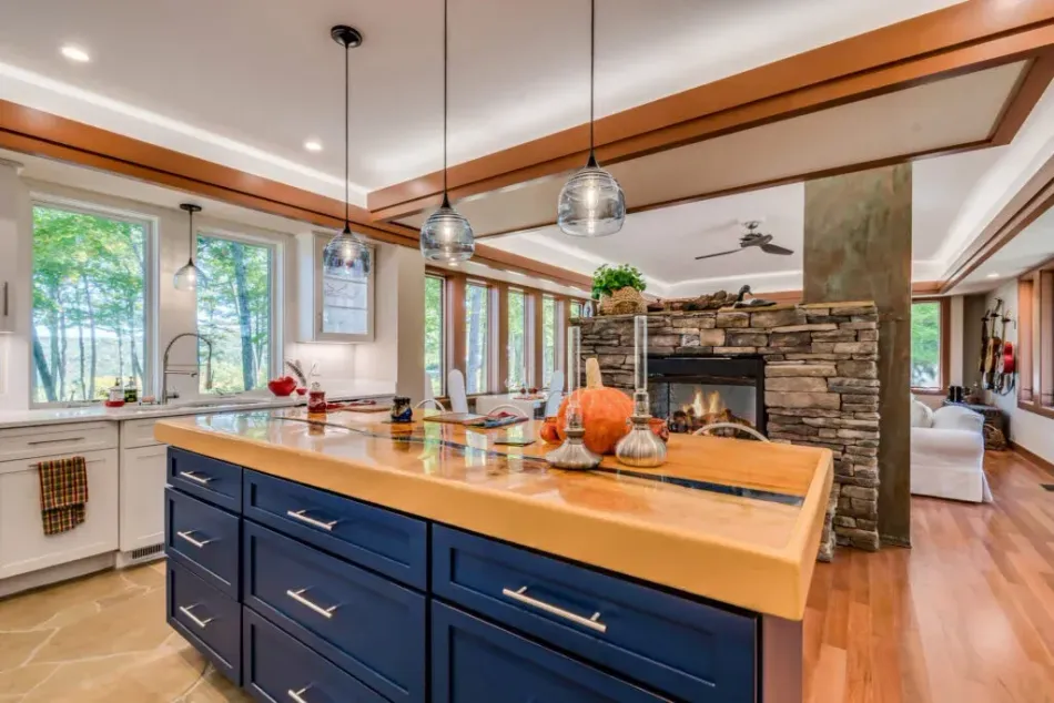 Modern kitchen with navy island, wooden countertop, pendant lights, and stone fireplace beyond