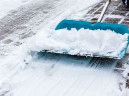 A bright blue snow shovel pushing a pile of white snow across a paved walkway.