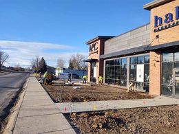 Workers in neon vests landscape the dirt ground in front of commercial brick buildings on a sunny day.
