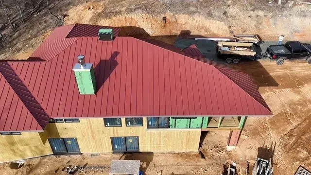 Red metal roof on a house under construction with wooden siding and a chimney.