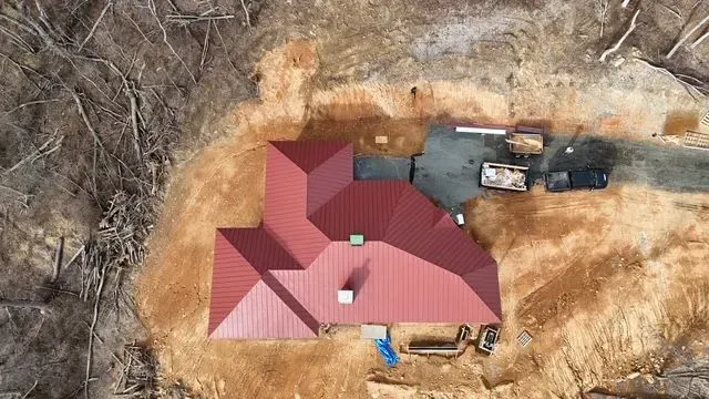 Overhead view of a red-roofed house under construction on a dirt lot, surrounded by bare trees.