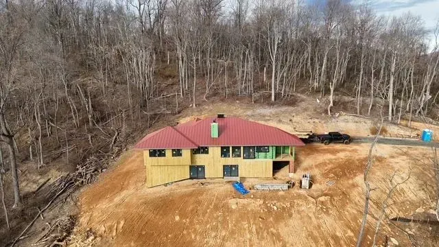 House under construction on a hillside with red roof and surrounding bare trees.