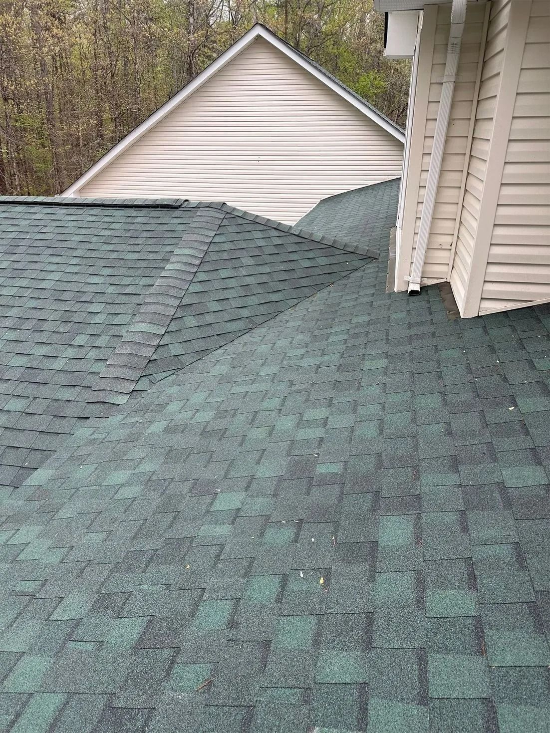 A green shingle roof intersection with beige siding and a triangular peak in the background.