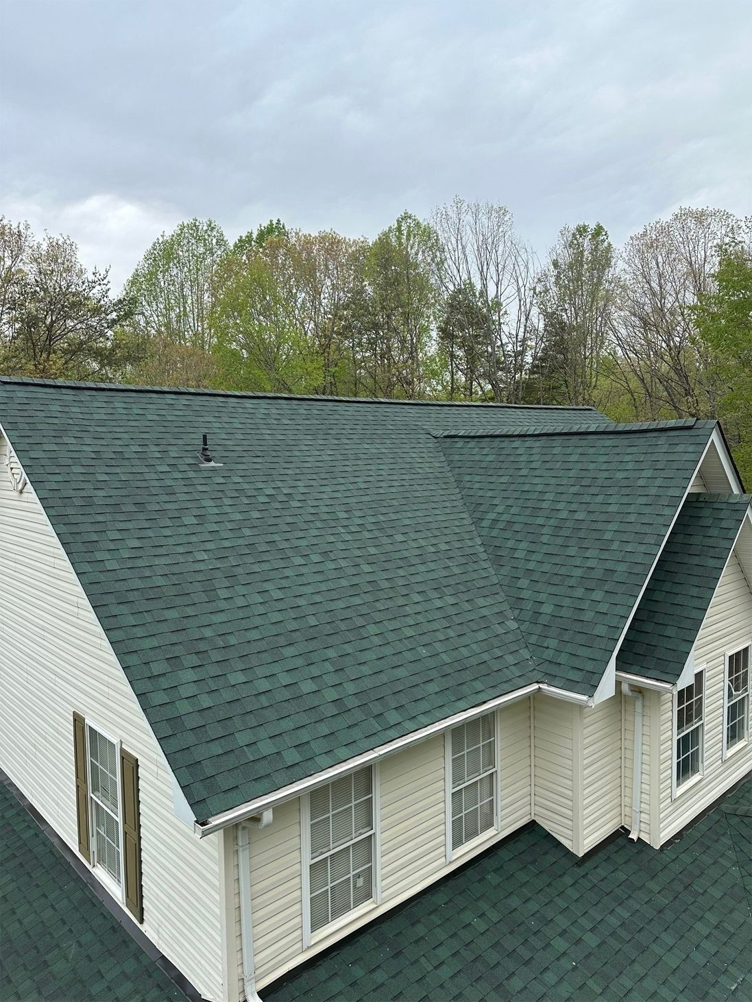 Green-roofed house with white siding, windows, and trees in the background under a cloudy sky.