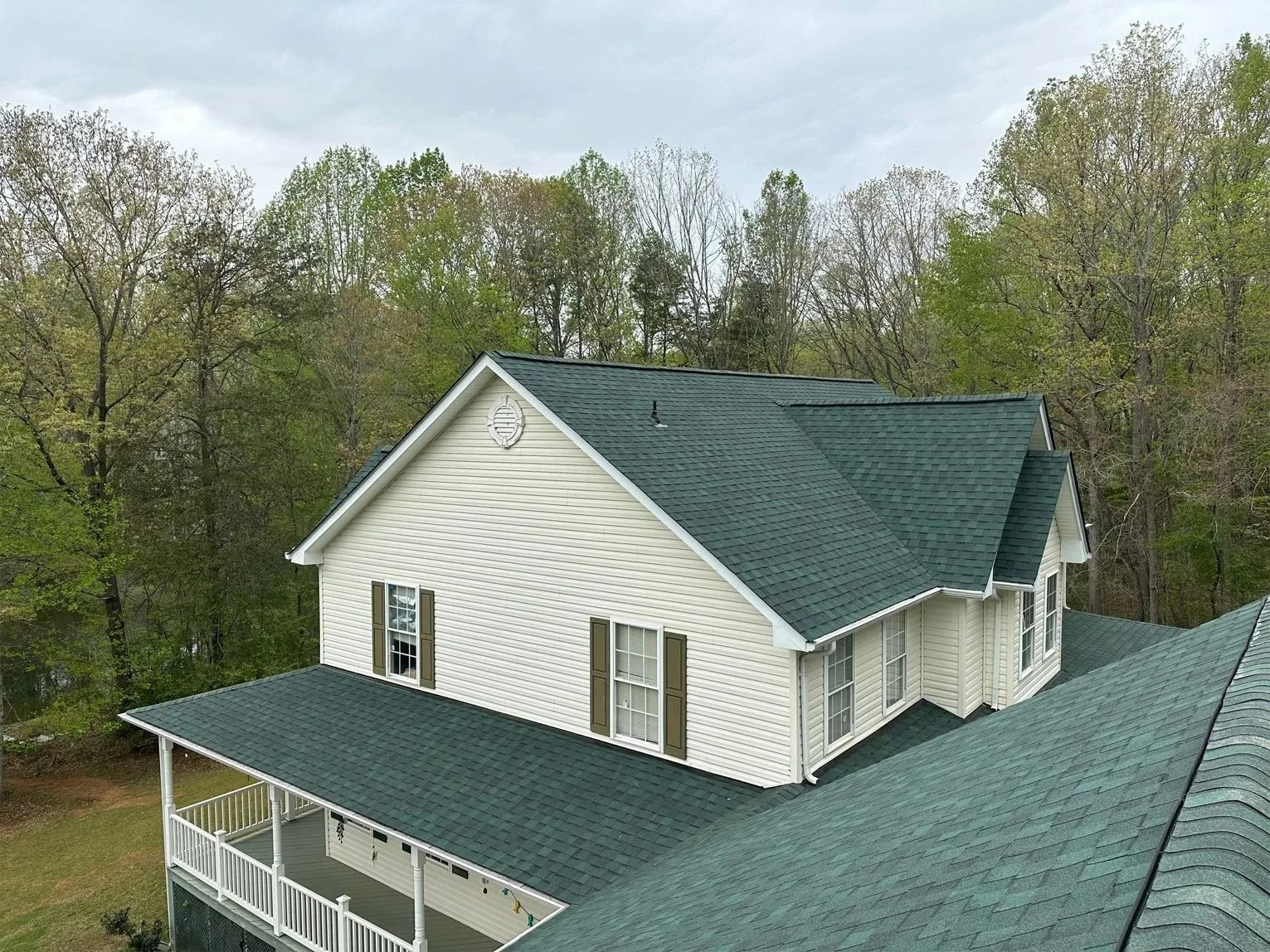Green-roofed white house with porch, surrounded by trees under an overcast sky.