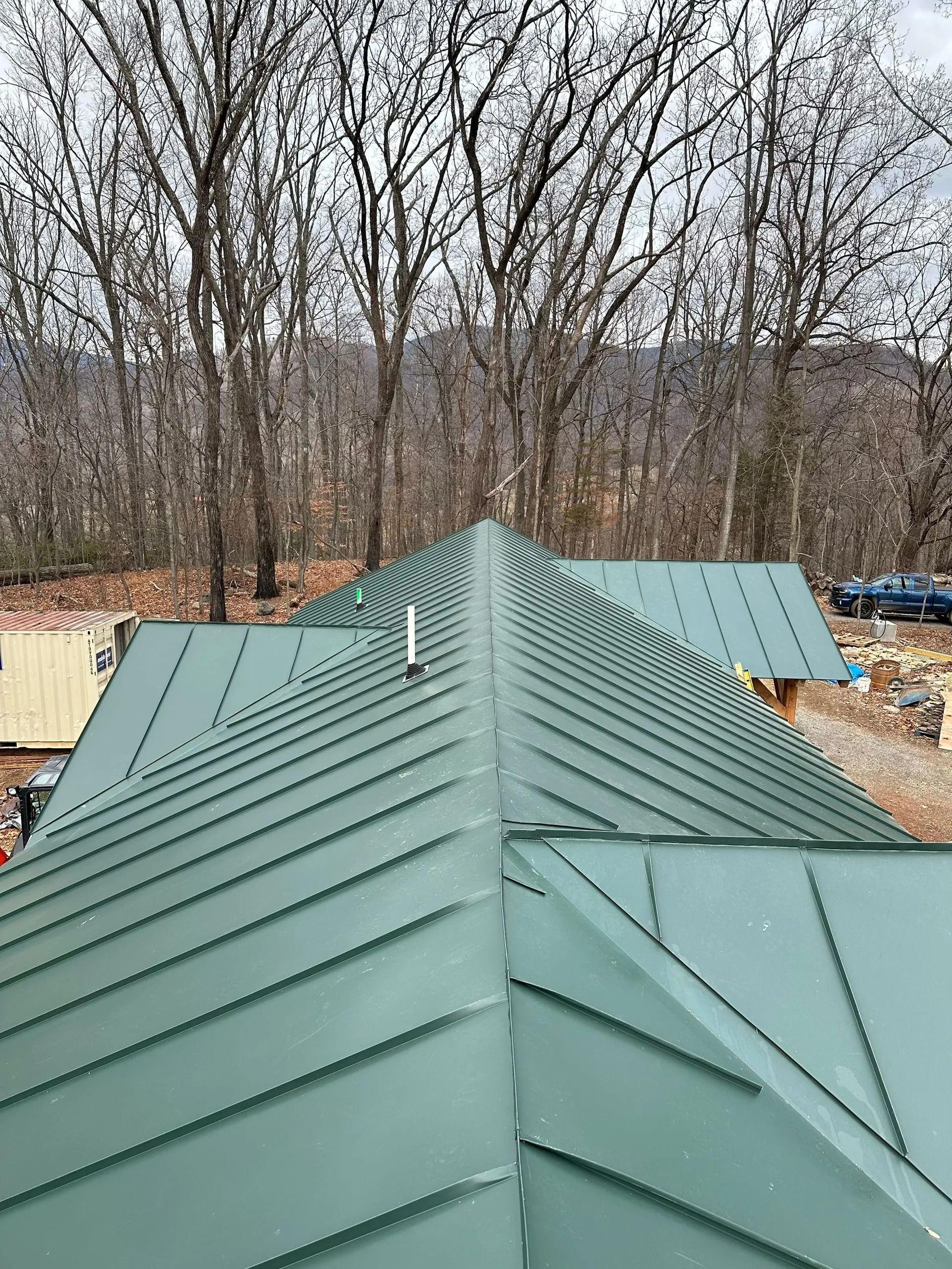 Green metal roof on a building in a wooded setting.