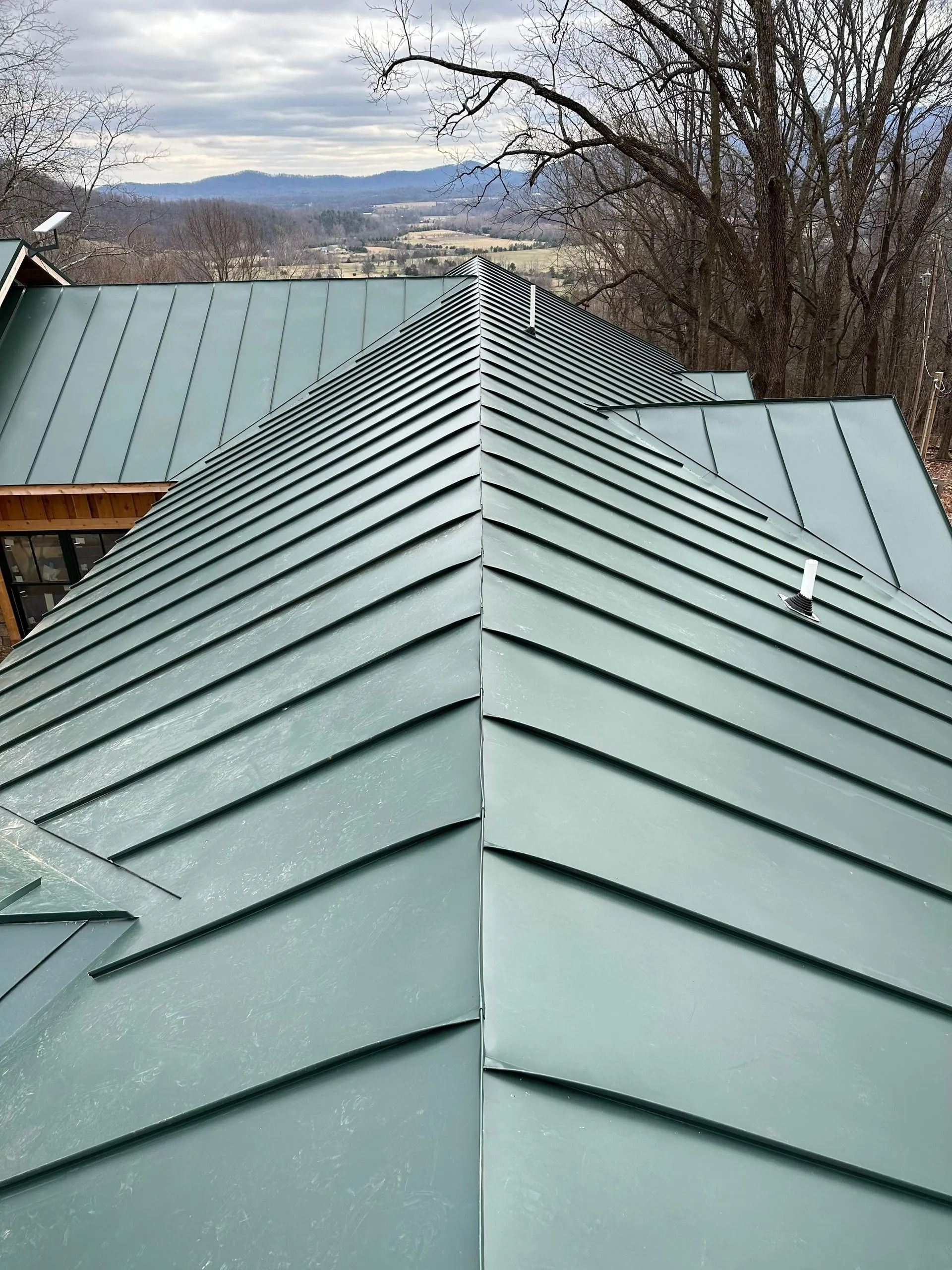 Green metal roof of a house with a valley and distant mountains visible.