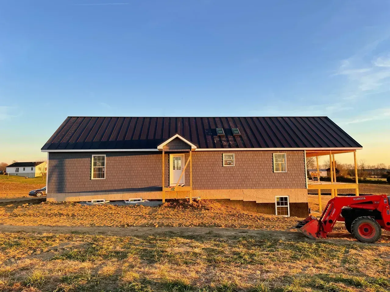 A newly built, single-story house with dark blue roof. A tractor and farmland are in the foreground.