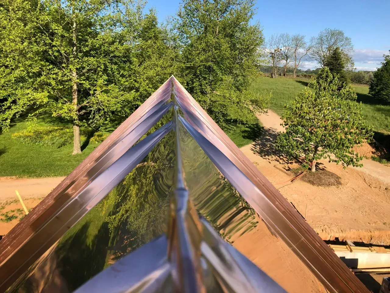 Copper roof ridge reflecting trees and a sunny landscape.