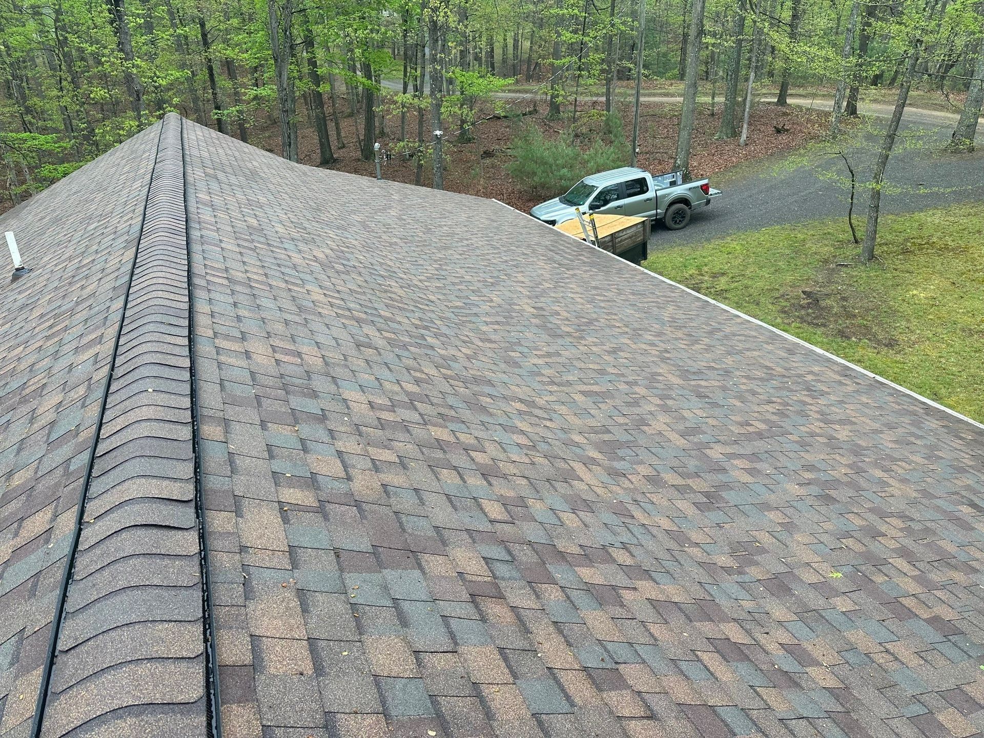 Roof with brown shingles, overlooking a driveway and trees.