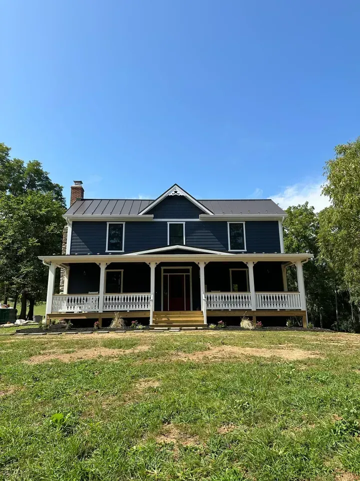 Blue farmhouse with white porch and roof against a clear blue sky.