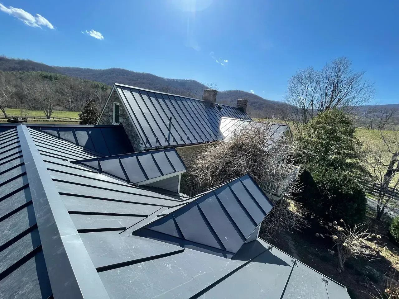 Dark gray metal roof on a building, sunny day with mountains in the background.