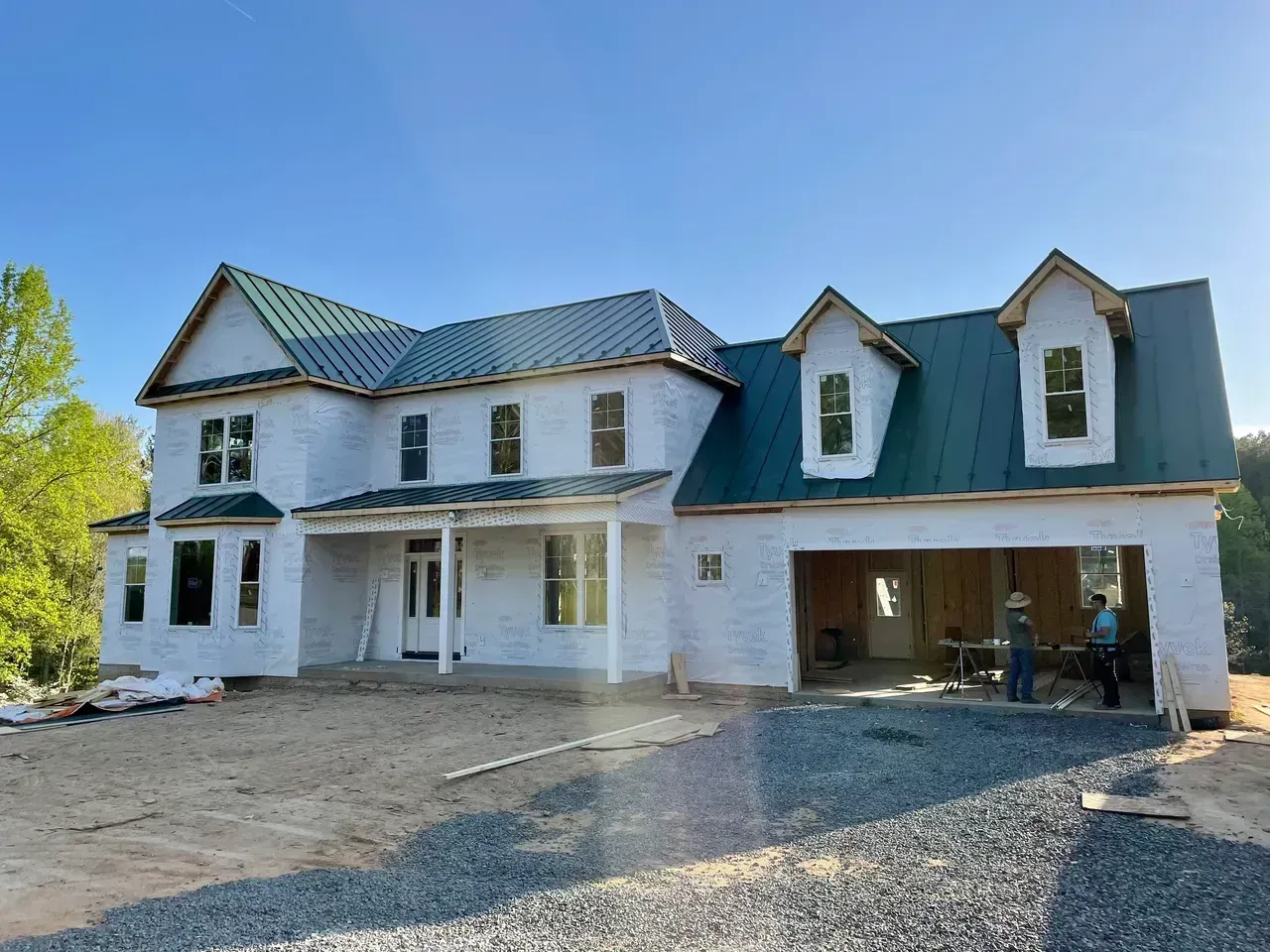 Construction of a two-story white house with a green roof and open garage under a blue sky.