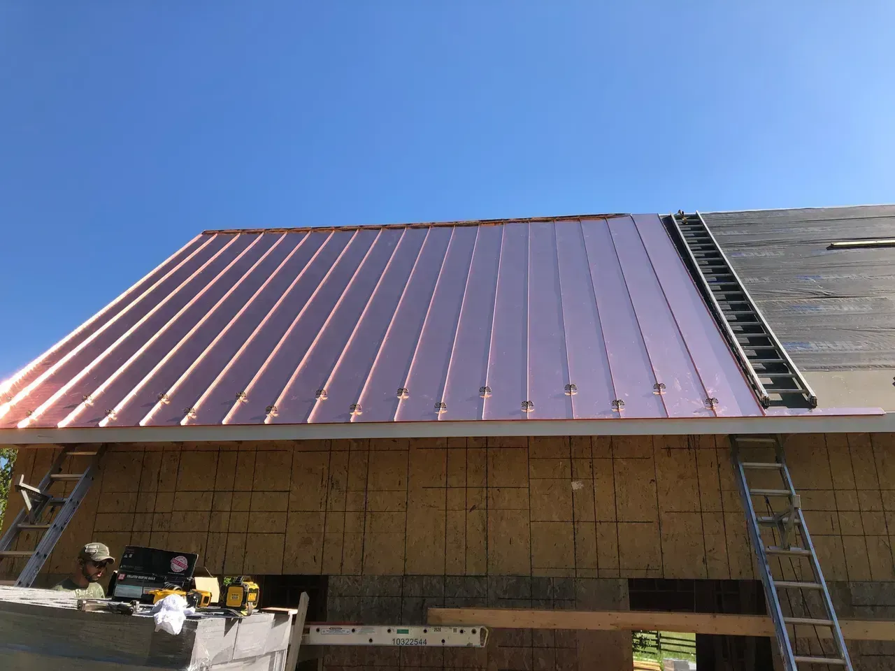 New copper roofing being installed on a wooden structure under a clear blue sky.