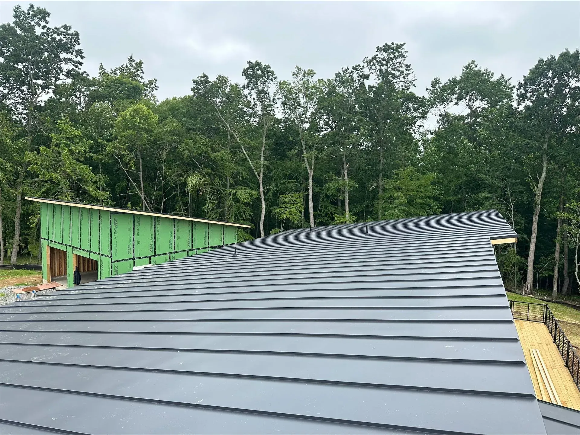 Metal roof under construction with green siding and trees in the background.