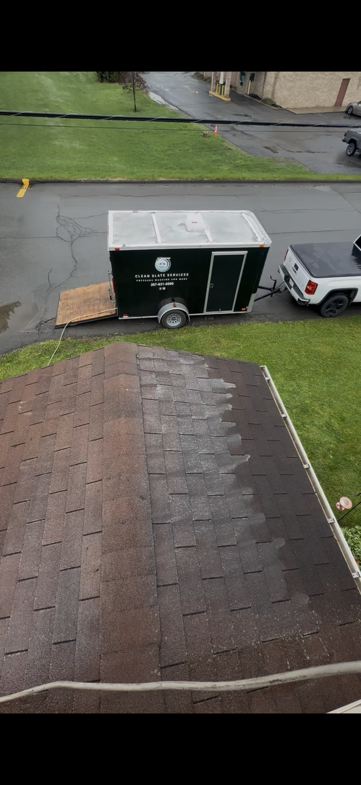 A dark-colored pickup truck towing a black flatbed trailer parked in an empty outdoor lot on an overcast day.