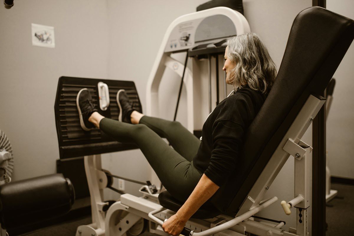 A person exercises on a leg press machine at a gym, with their feet pushing against the elevated weight plate.