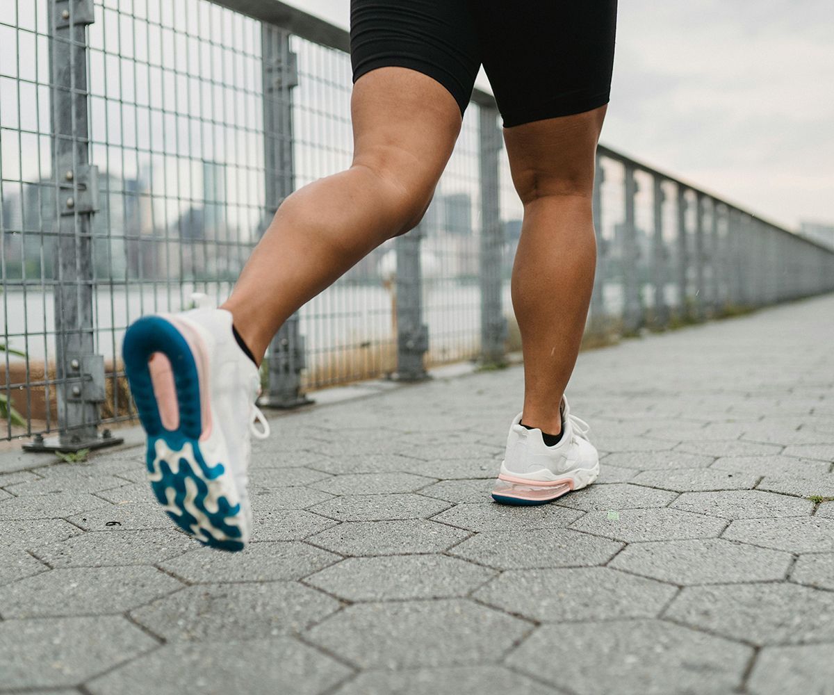 Person running on a paved path, wearing white running shoes and black shorts.