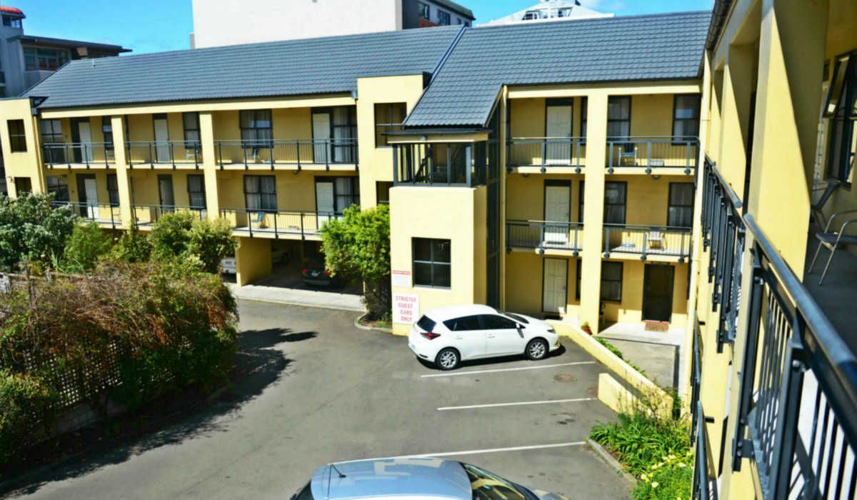 A white van is parked in front of a large yellow building.