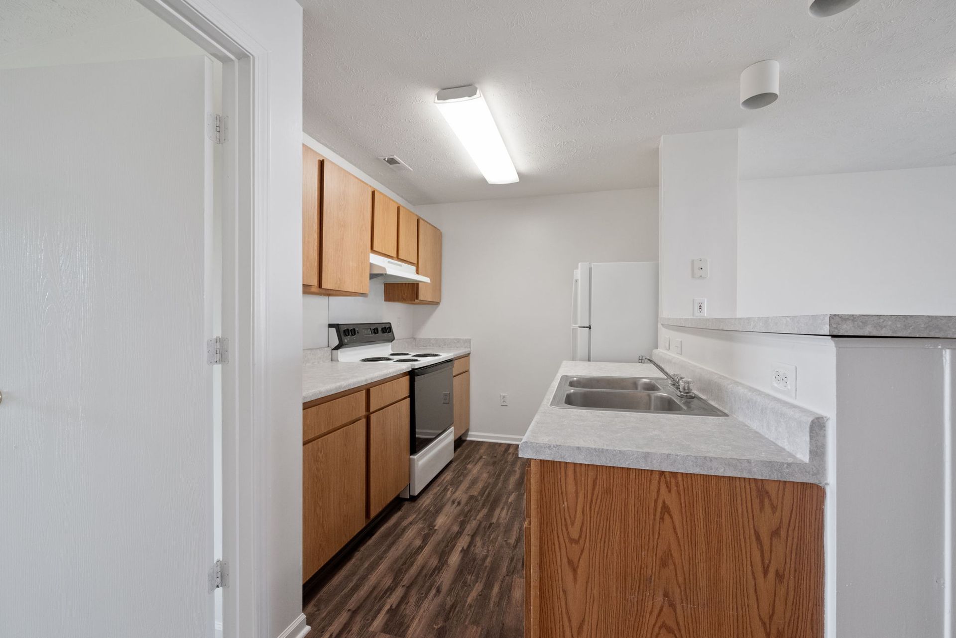 A kitchen with wooden cabinets , a stove , a refrigerator , and a sink.