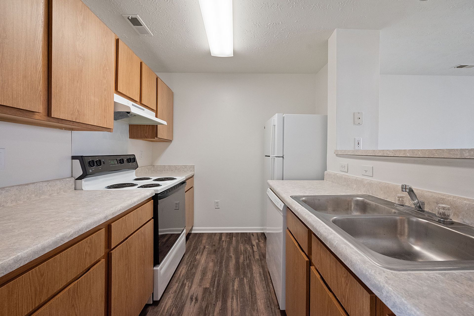 A kitchen with wooden cabinets , a stove , a sink , and a refrigerator.