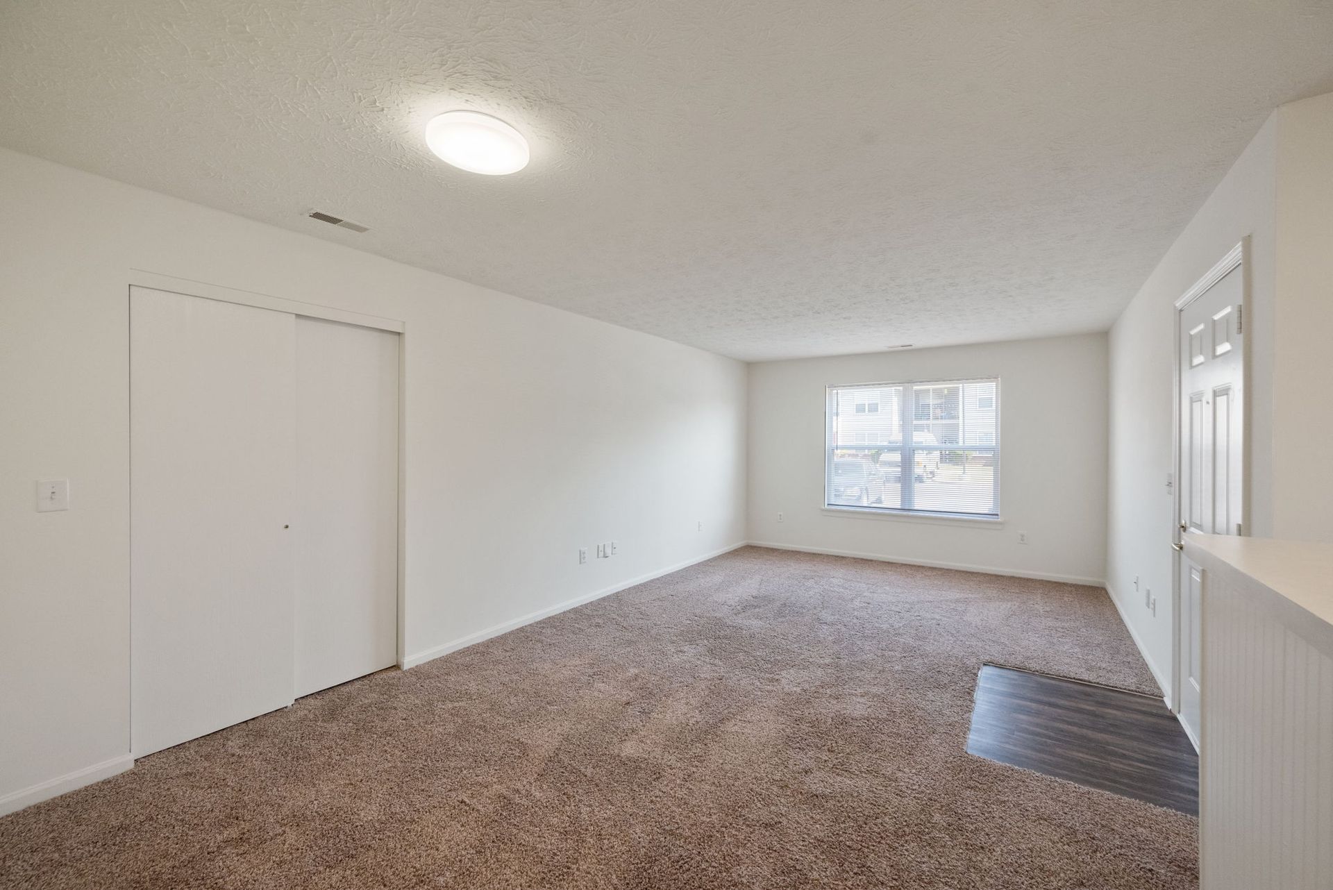 An empty living room with a carpeted floor and a window.