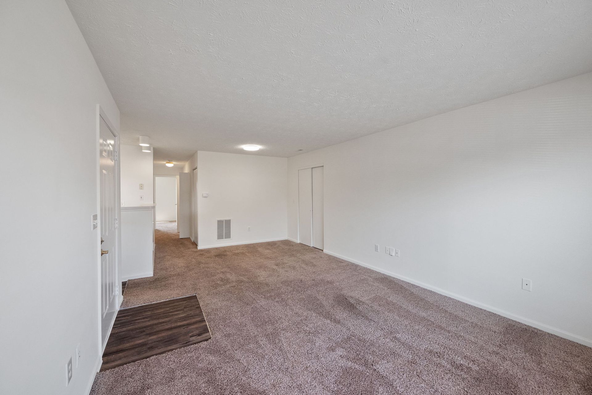 An empty living room with a carpeted floor and white walls.
