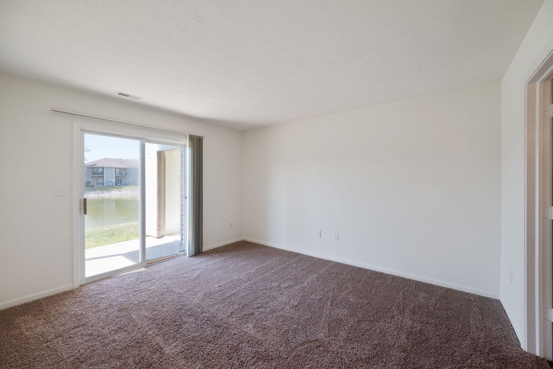 An empty living room with a sliding glass door and a brown carpet.