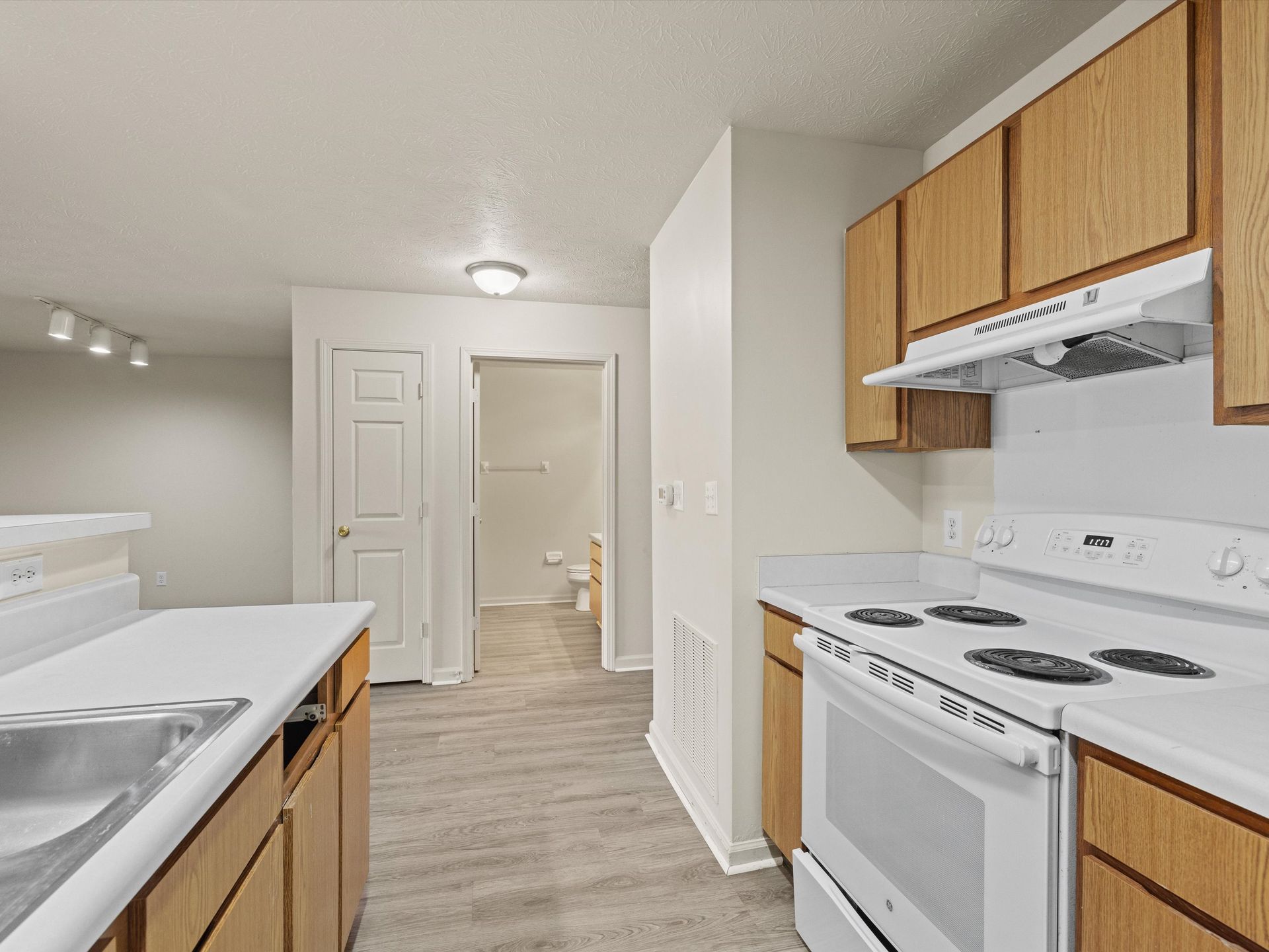 A kitchen with a stove , sink , and cabinets, and view of bathroom.