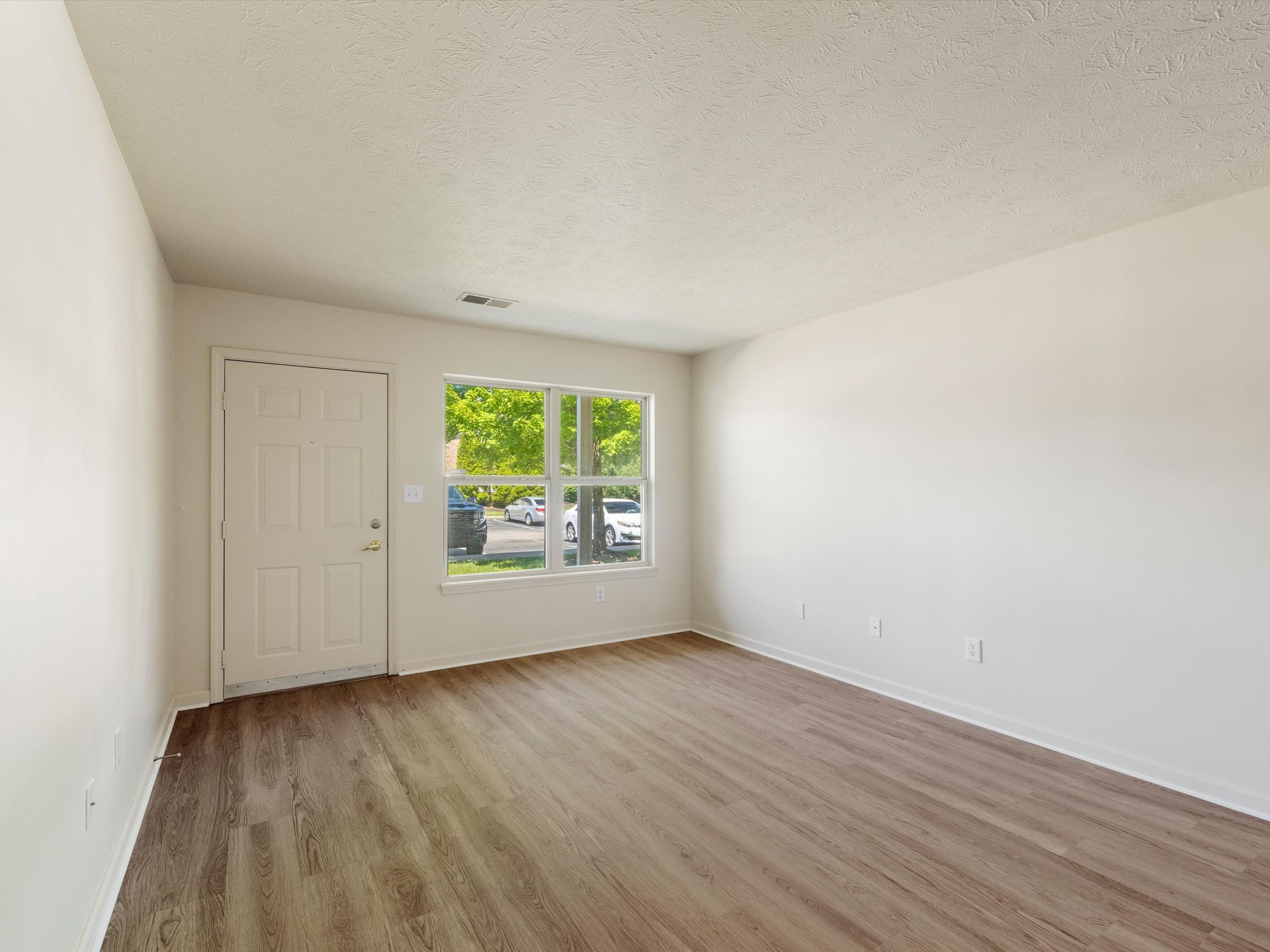 An empty living room with hardwood floors and white walls.