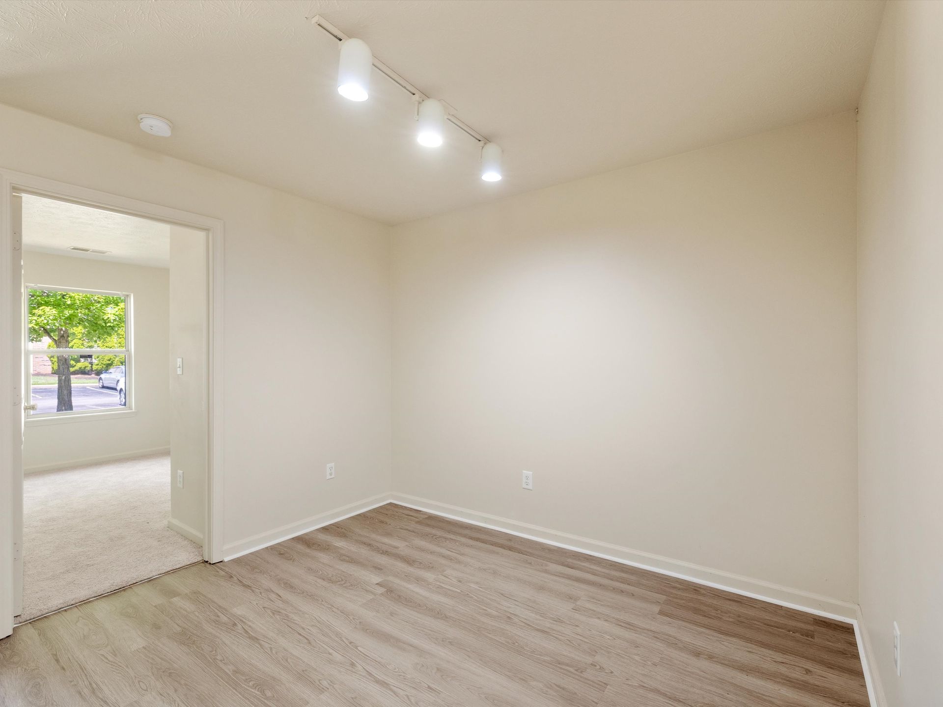 An empty room with hardwood floors , white walls and a window.