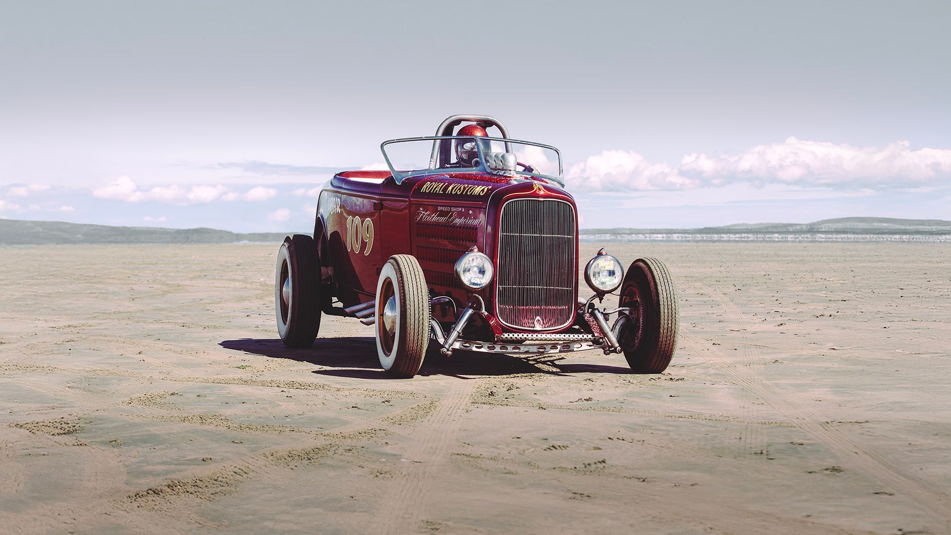 A red hot rod on a beach shot by Dammo Photography