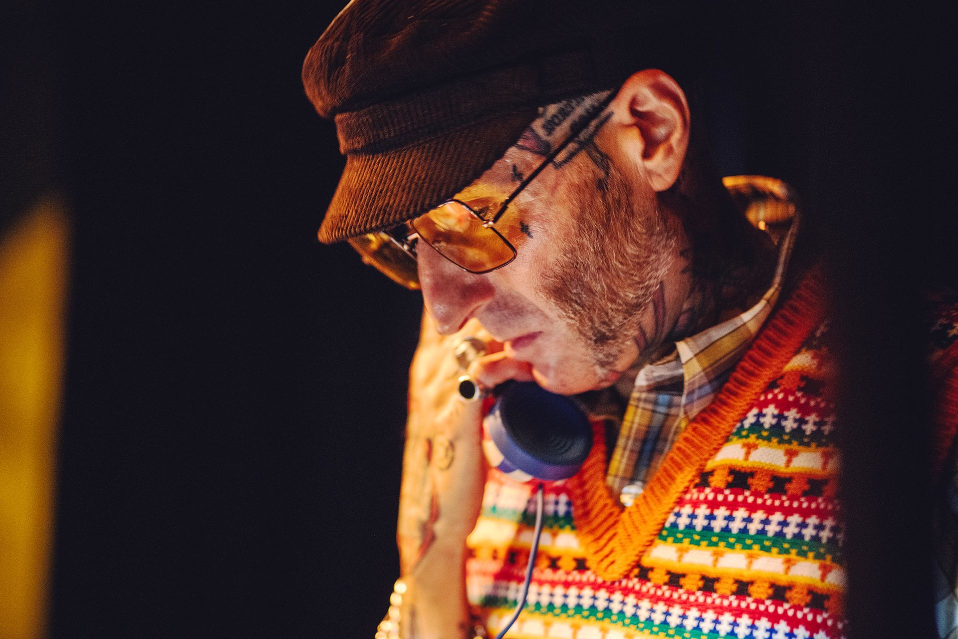 A man dressed in colourful vintage clothing using an old fashioned telephone mouth piece to que up records on a turntable shot by Dammo Photography