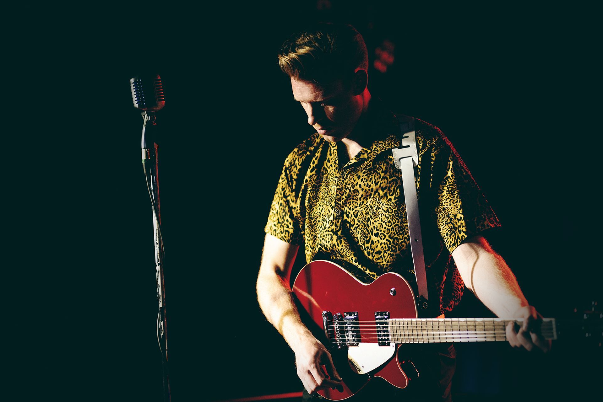 A man in a yellow shirt is playing a red guitar in front of a microphone shot by Dammo Photography