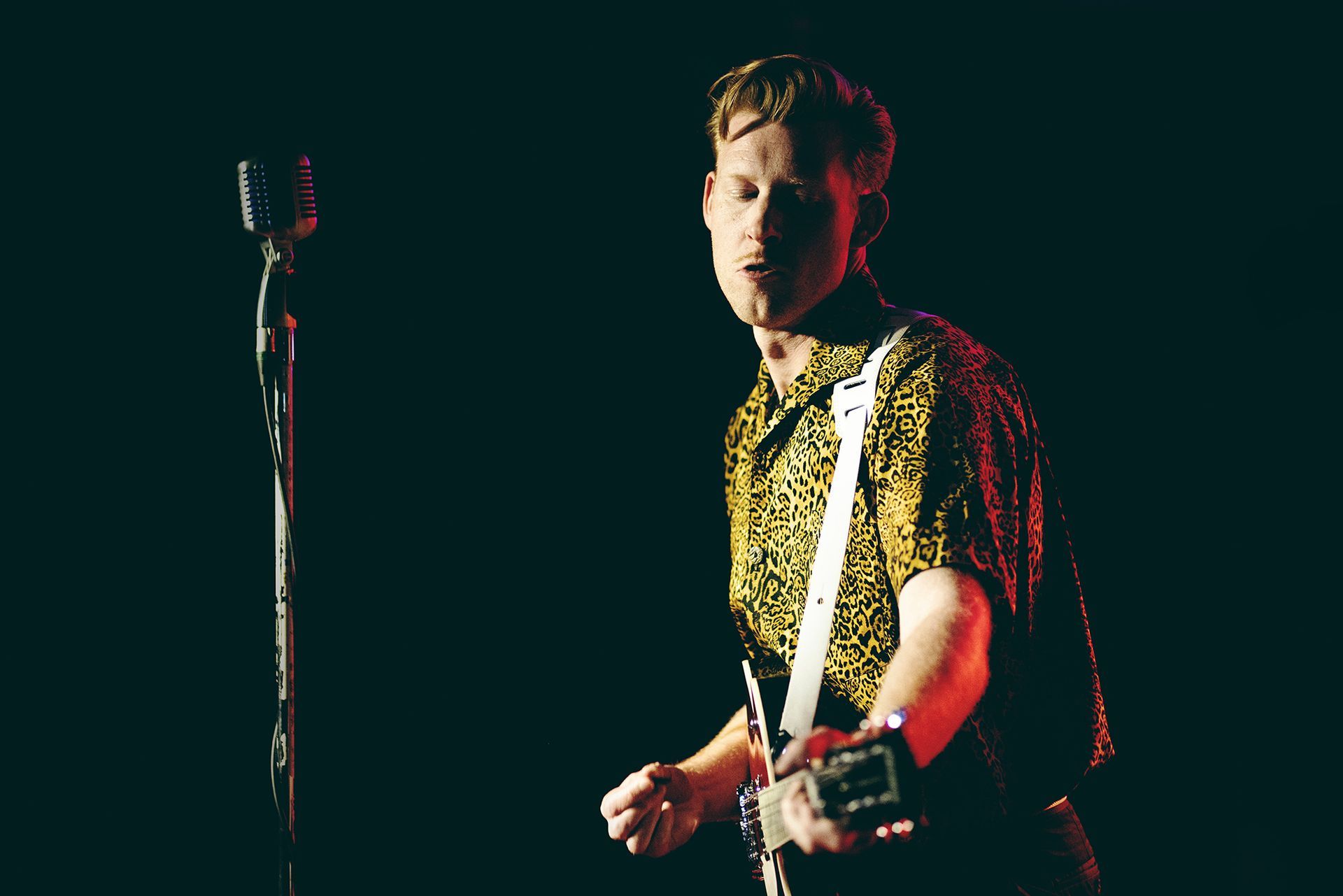 A man is playing a guitar and singing into a microphone on a stage shot by Dammo Photography