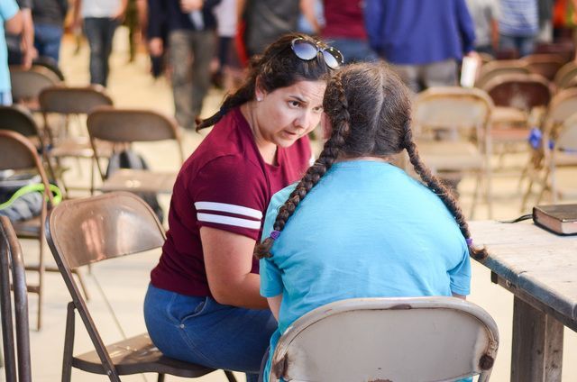 Two people talking at a table in a cafeteria, with one wearing a red shirt and the other a blue shirt.