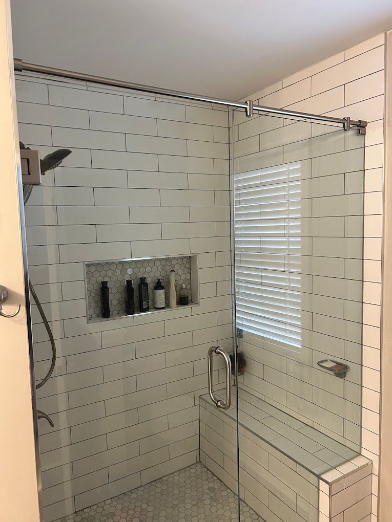 A bathroom with white tiles and a walk in shower with a glass door.