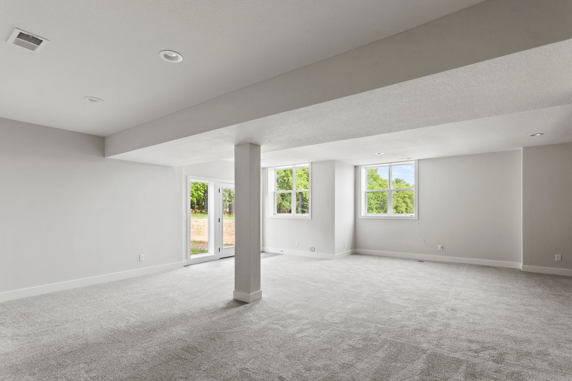Basement room with white walls, support beams, and a carpeted floor, with doorways leading to other areas.