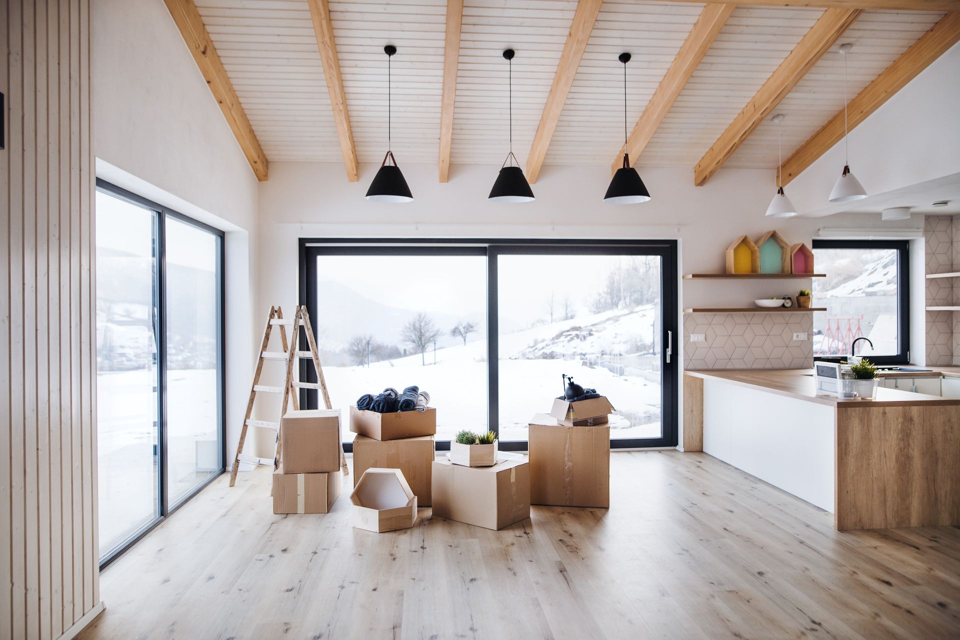 Interior of a room with moving boxes, large windows looking out onto a snowy landscape, and pendant lights.