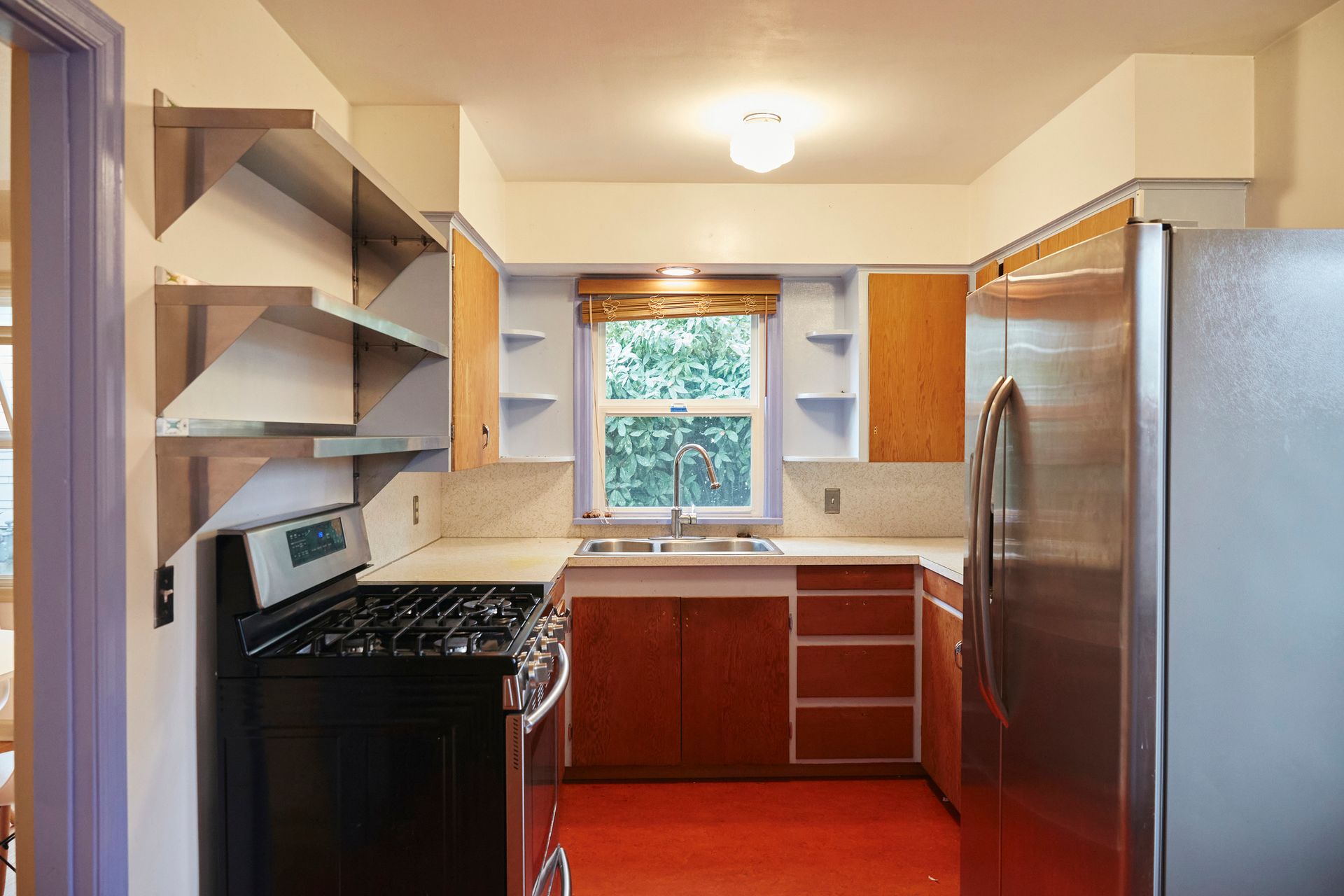 U-shaped kitchen with red floor, wooden cabinets, stainless steel fridge, and gas stove.