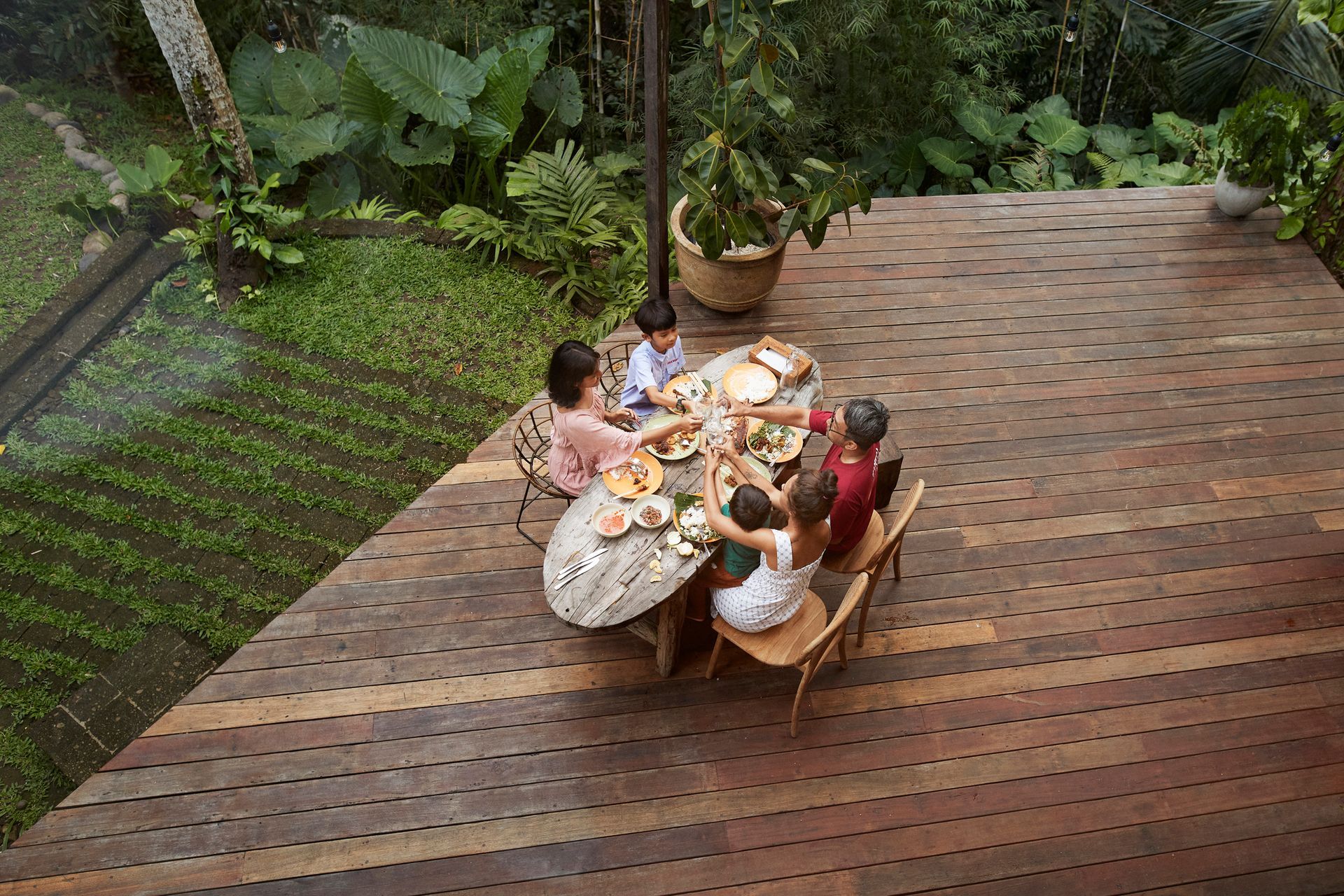 Family eating at a wooden table on a deck overlooking a lush green landscape.