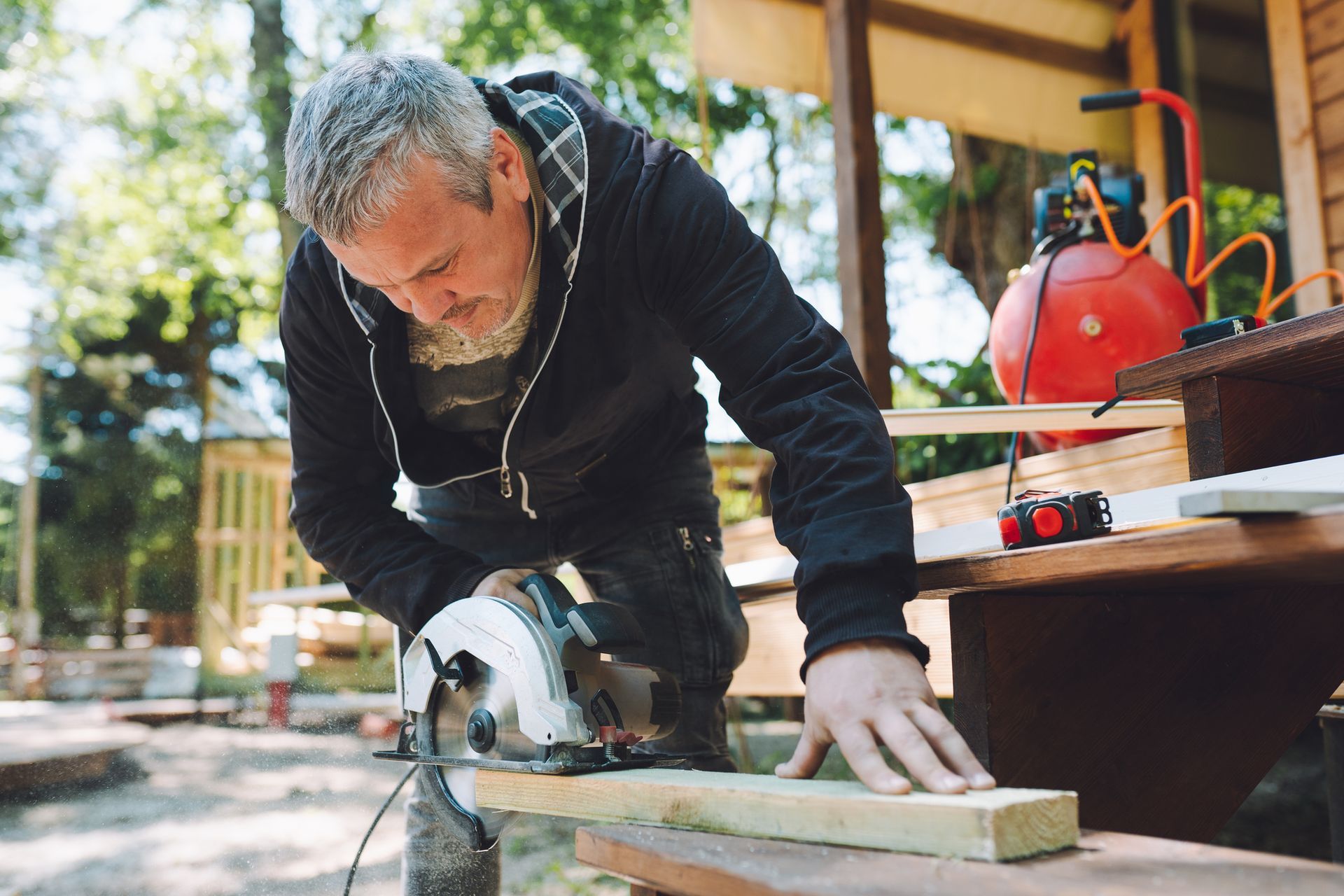 Man using a circular saw to cut a wooden plank outdoors.