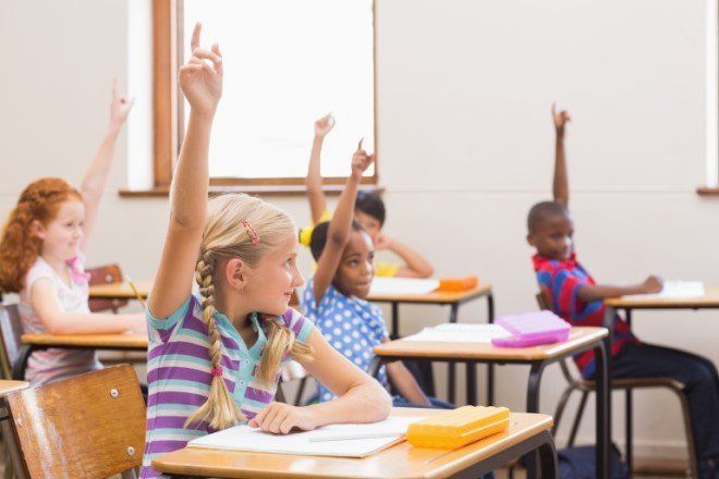 Children in a classroom raising hands to answer a question.