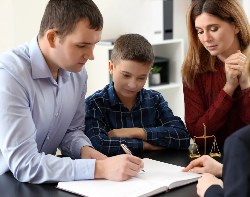 Family at a table signing documents with a legal professional; scales of justice visible.