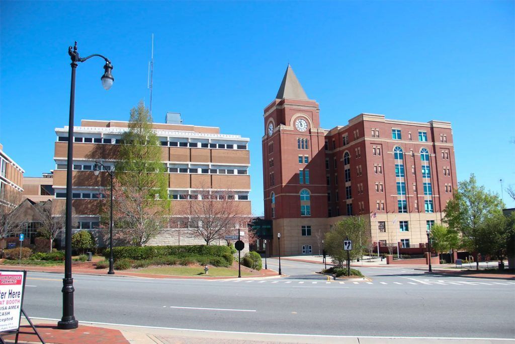 Two brick buildings and a utility building on a sunny day. A lamppost is in the foreground.
