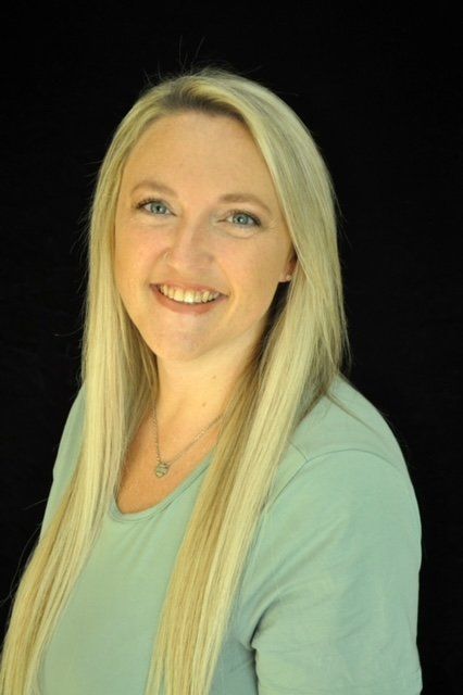 Blonde woman smiling, wearing a light green shirt, against a black background.